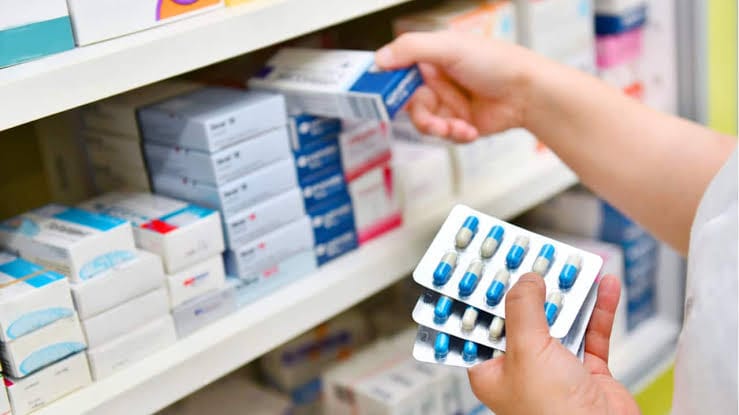 Person holding a pack of blue pills in a pharmacy