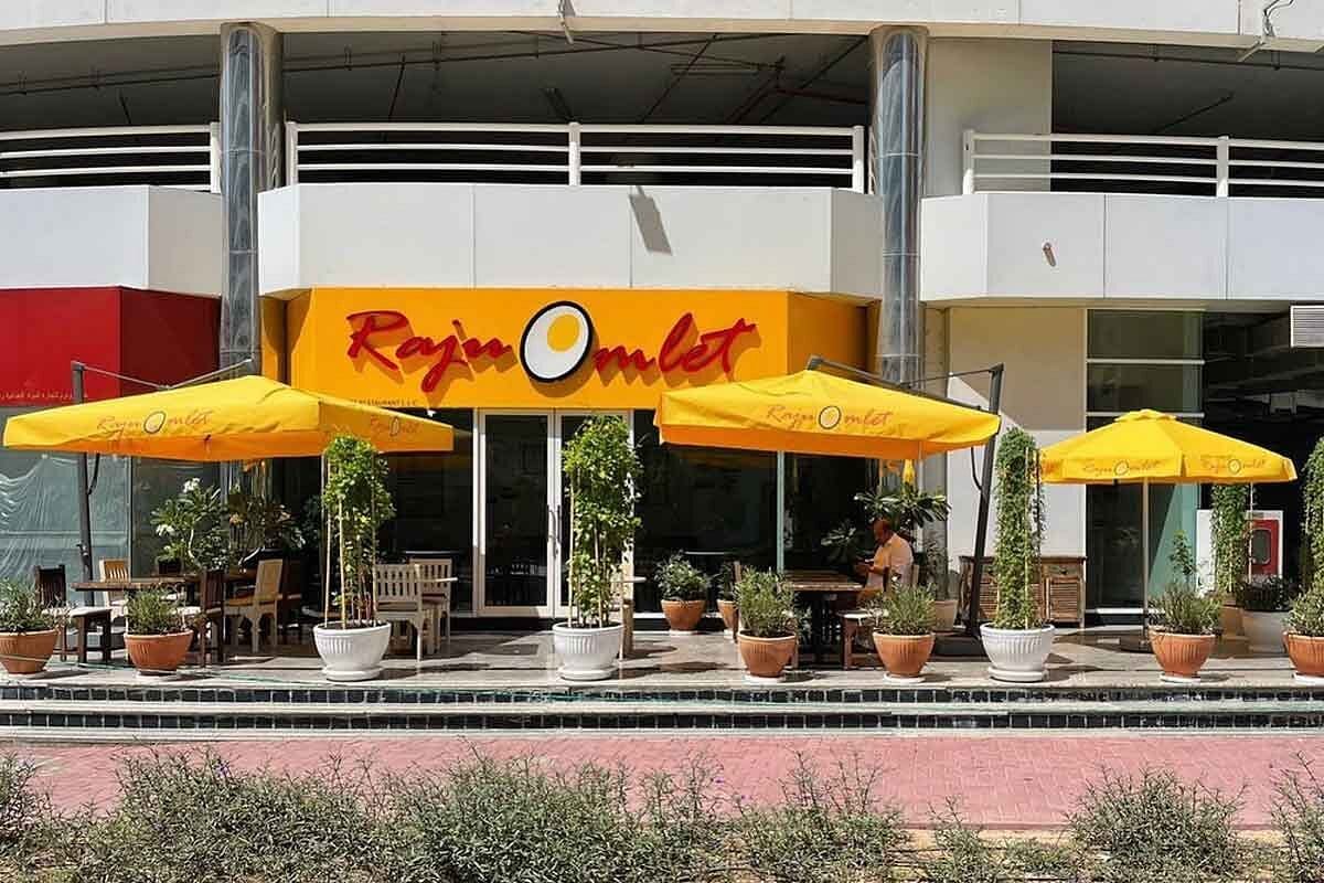 Raju Omlet restaurant exterior with yellow umbrellas and outdoor seating.
