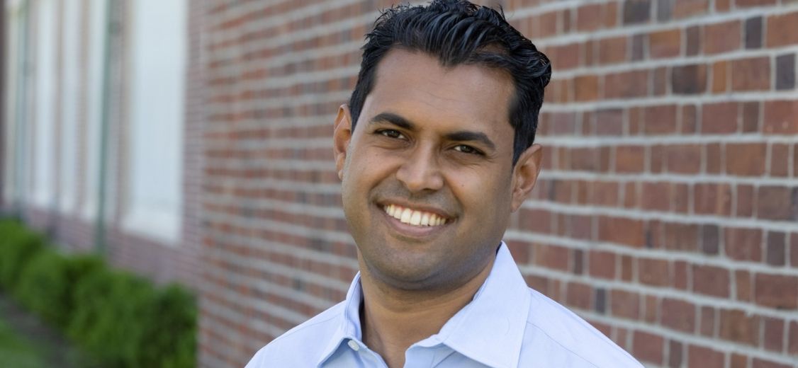 Vin Gopal smiles in front of a brick building, celebrating new beach safety law.