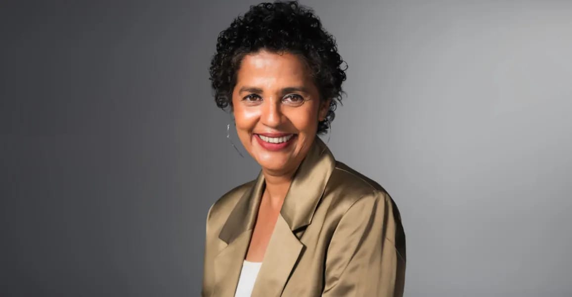 Indian American CEO smiles in a gold blazer, supporting women's scholarships.