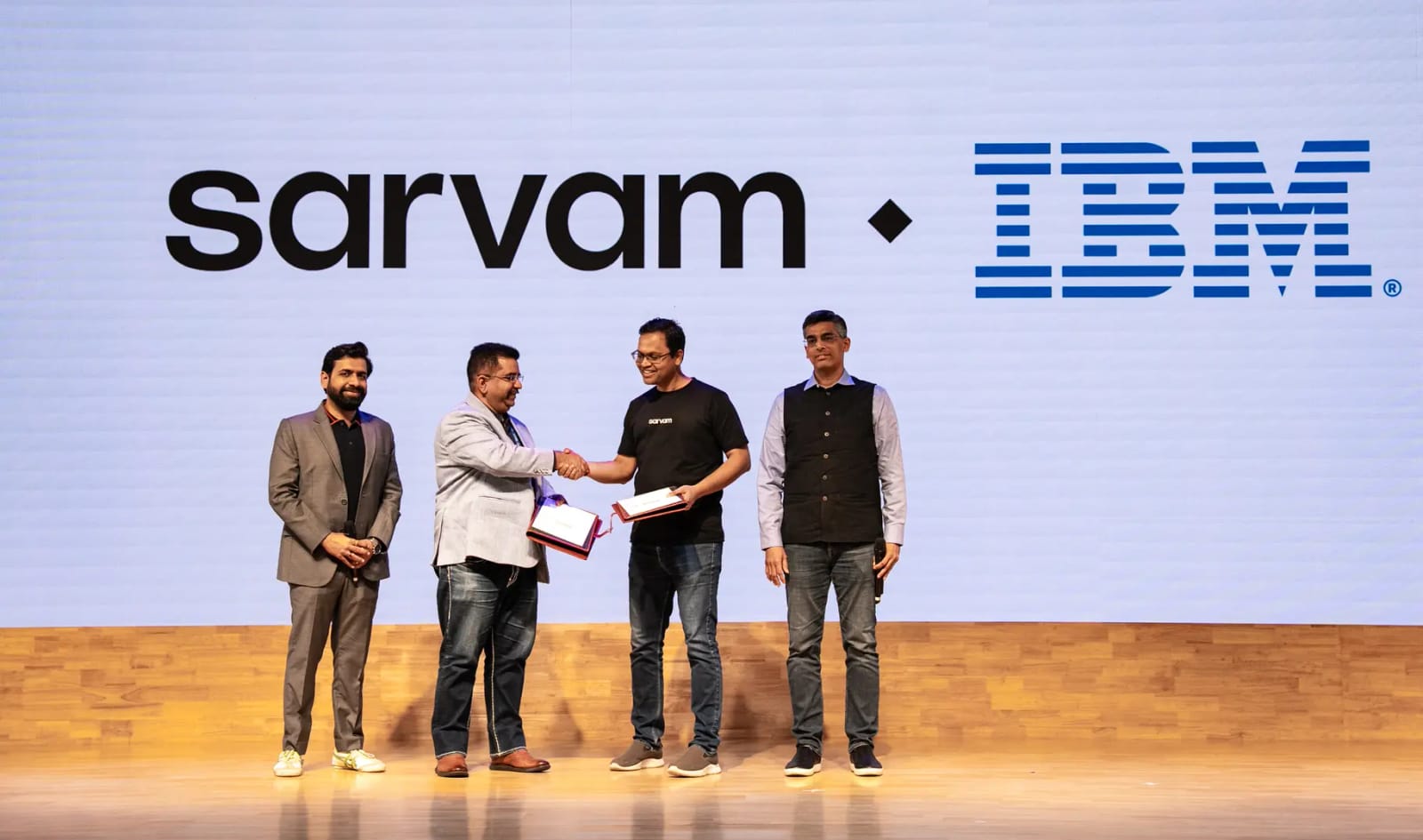 IBM and Sarvam leaders shake hands, signifying a tech partnership for India's AI projects.