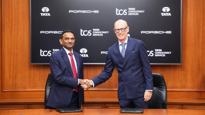 TCS executives shake hands in front of Porsche and TCS logos.