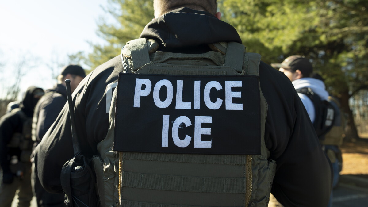 ICE officer in police vest walking among crowd, "Police ICE" on back